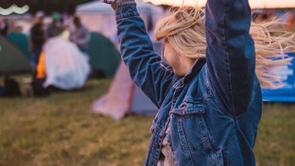 A woman with her hands in the air in front of a campsite at a festival