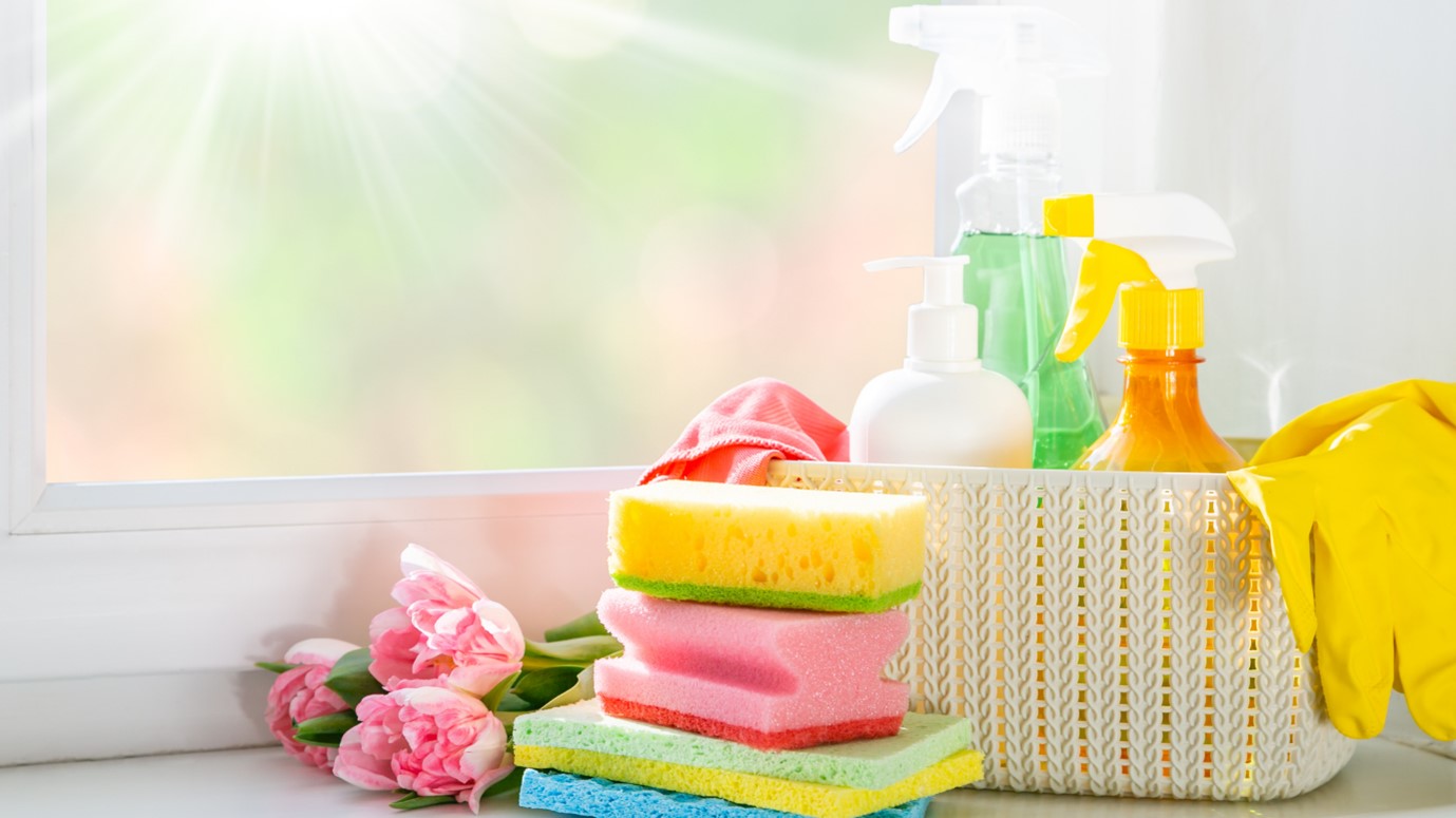 Image of cleaning products including sponges, cleaning spray and rubber gloves next to a sunny spring window