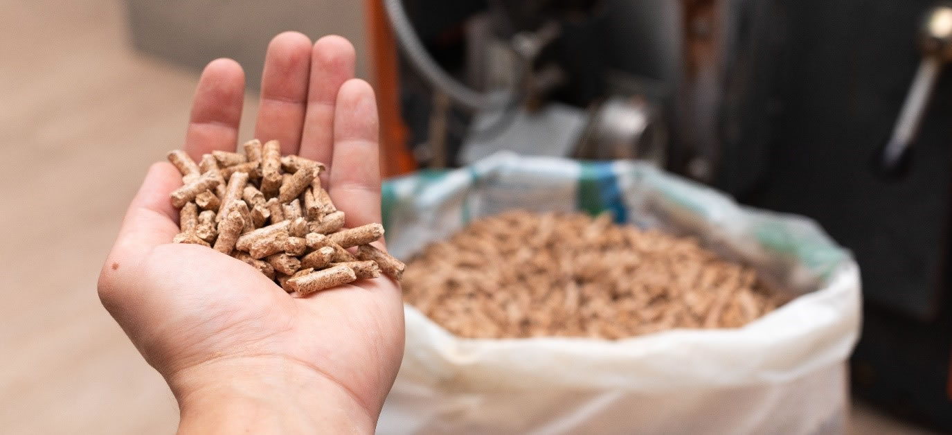  A hand holding wood pellets in front of a wood pellet bag and heating system.