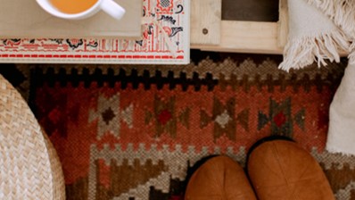 An image of slippers on a rug, with a cup of tea at the side. Banner says “Clever Ways to Warm Up Your Home Without Using the Thermostat”